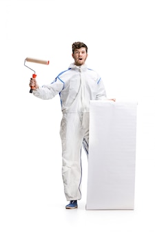 Young male decorator painting with a paint roller isolated on white wall.
