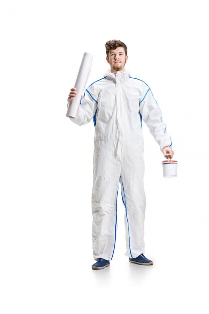 Young male decorator painting with a paint roller on white wall.