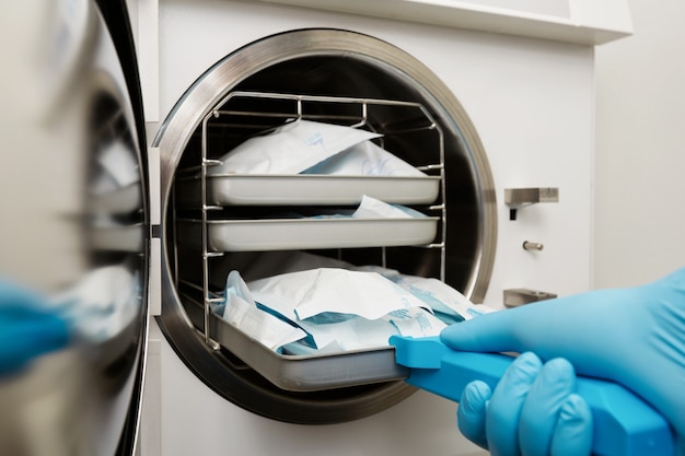 Young male dentist places medical autoclave for sterilising surgical and other instruments