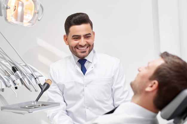 Young male dentist smiling at his patient during medical appointment