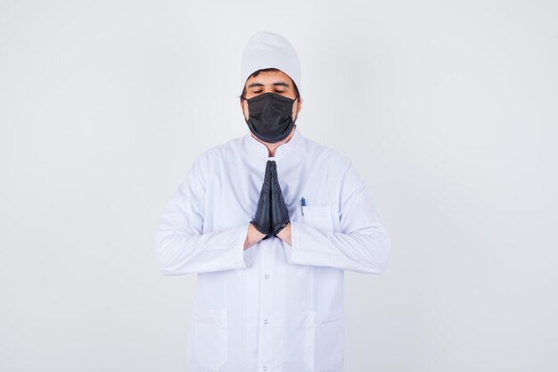 Free photo young male doctor showing namaste gesture in white uniform and looking peaceful. front view.