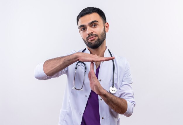 young male doctor wearing stethoscope medical gown showing timeout gesture on isolated white wall