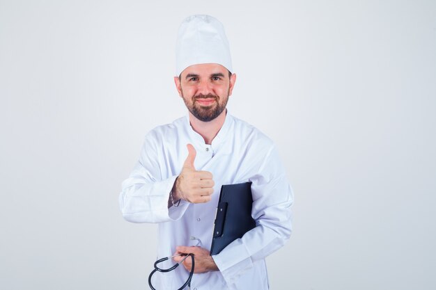 Young male doctor in white uniform holding clipboard, stethoscope, offering handshake as greeting and looking gentle , front view.
