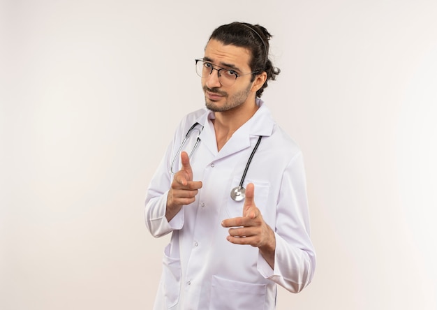 あなたにジェスチャーを示す聴診器で白いローブを身に着けている光学メガネを持つ若い男性医師