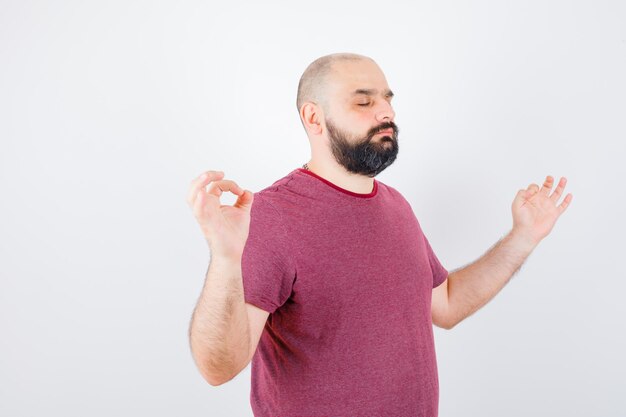 Young male doing meditation in pink t-shirt and looking focused .