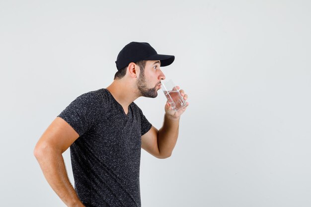 Молодой мужчина пьет воду в футболке и кепке и выглядит жаждущим