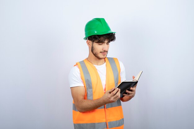 Young male engineer in green hardhat reading notes on white background. High quality photo