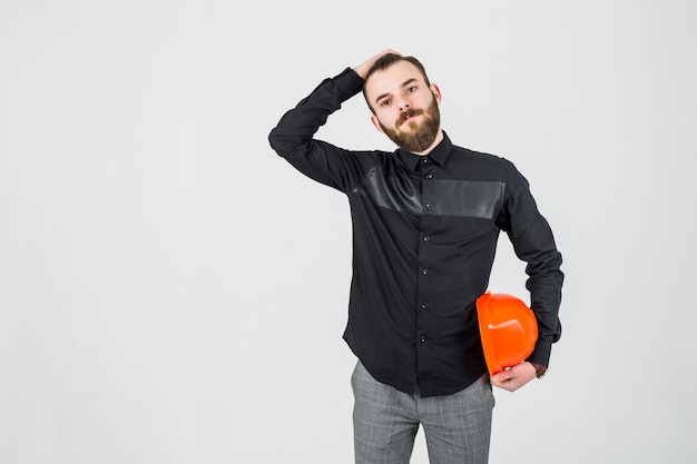 Young male engineer with hand on his head holding hardhat