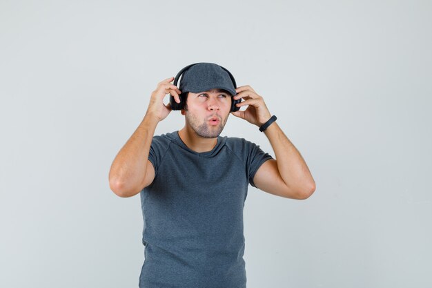 Young male enjoying music with headphones in t-shirt cap and looking pensive 