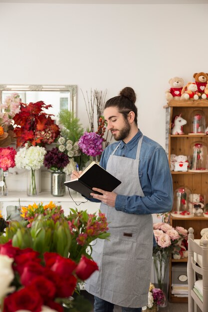 ペンで日記を書くフラワーショップに立っている若い男性の花屋