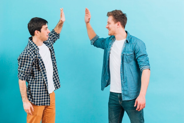 Young male friend giving high five against blue background