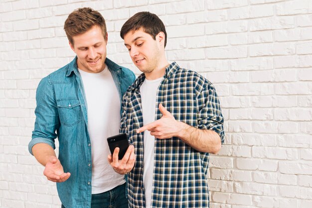 Молодые друзья-мужчины, показывая что-то на мобильный телефон своему другу