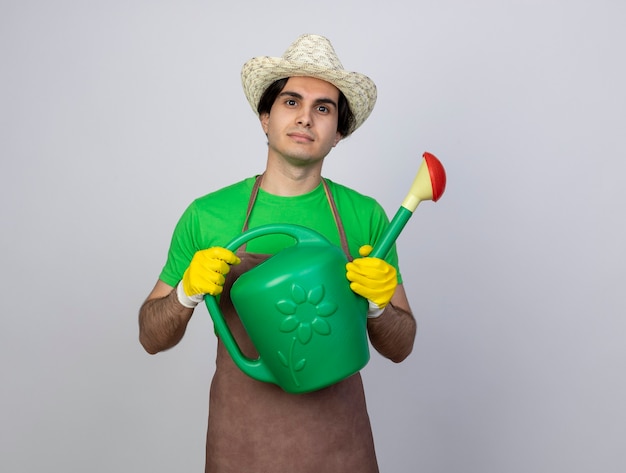 Young male gardener in uniform wearing gardening hat holding watering can -