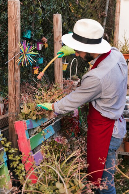 Young male gardener watering the plant with hose