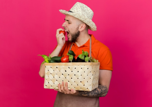 ガーデニング帽子をかぶって若い男性の庭師は野菜のバスケットを保持します