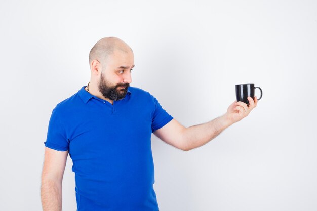 Foto gratuita giovane maschio che dà tazza a qualcuno in camicia blu e sembra soddisfatto.