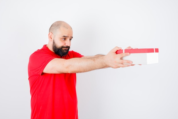 Young male giving present box to someone in red shirt and looking sorrowful .