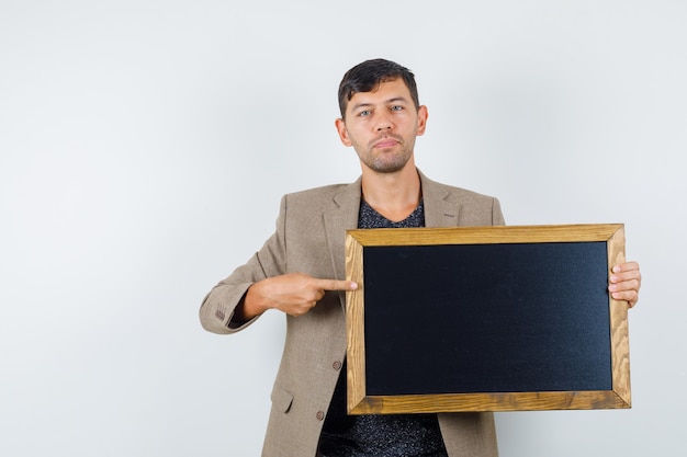 Young male in grayish brown jacket,black shirt pointing to cardboard and looking ready , front view.