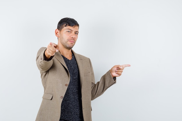 Free photo young male in grayish brown jacket,black shirt pointing at front and at copyspace