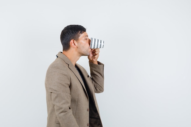 Young male in grayish brown jacket drinking water and looking thirsty