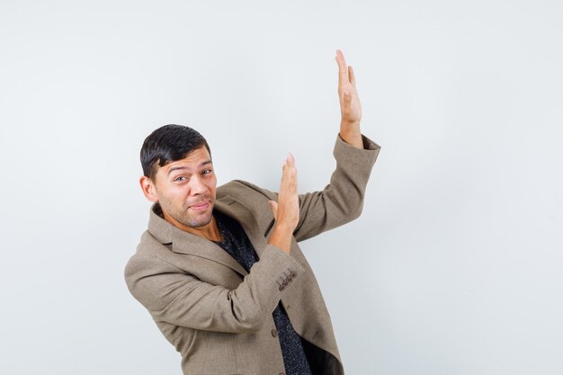 Young male in grayish brown jacket showing stop gesture aside while looking right and looking worried , front view.