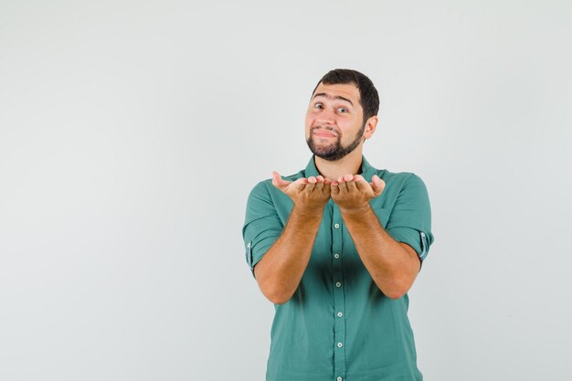 Young male in green shirt combining his hands with questioning manner , front view.