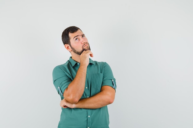 Giovane maschio in camicia verde che guarda lontano e sembra pensieroso, vista frontale.