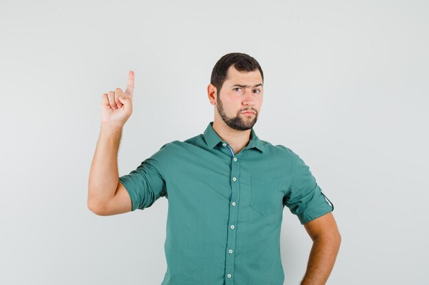 Young male in green shirt pointing up and looking strict , front view.