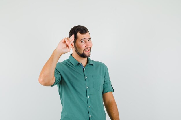 Young male in green shirt showing goodbye gesture and looking calm , front view.