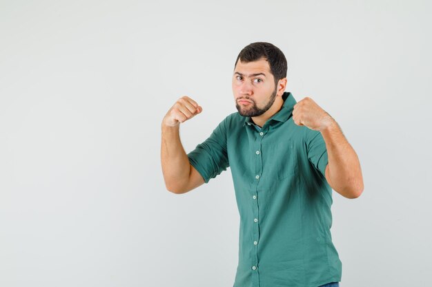 Молодой мужчина в зеленой рубашке показывает кулаки и выглядит агрессивно, вид спереди.