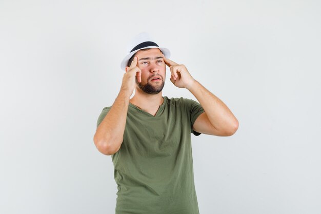 Young male in green t-shirt and hat holding fingers on temples and looking exhausted