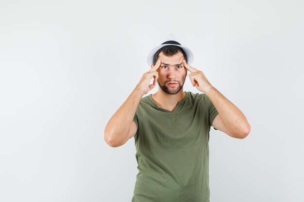 Young male in green t-shirt and hat holding fingers on temples and looking pensive