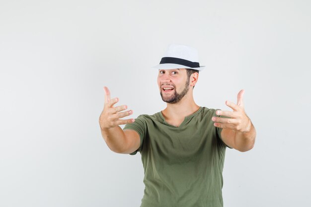 Young male in green t-shirt and hat inviting to come and looking cheerful