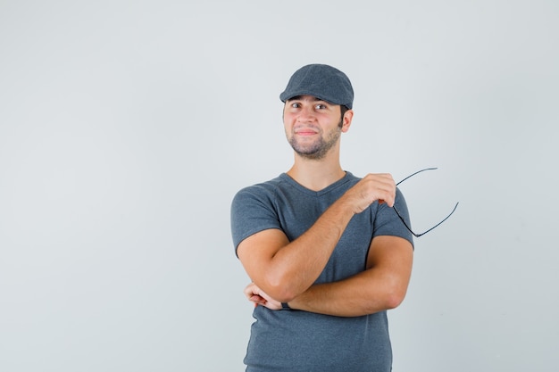 Young male in grey t-shirt cap holding glasses and looking confident  