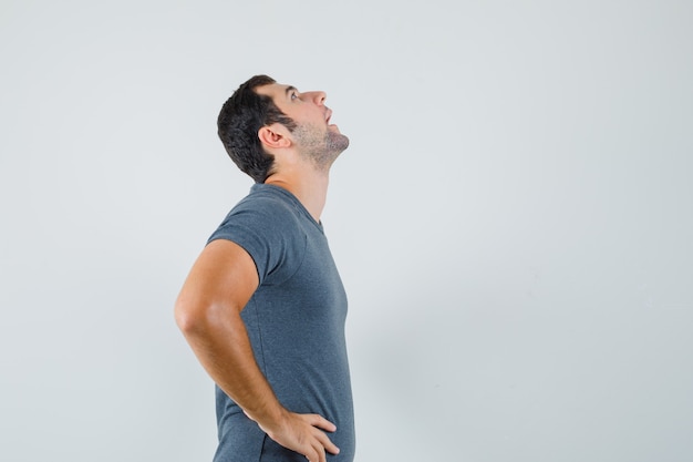 Young male in grey t-shirt holding hands on waist and looking patient