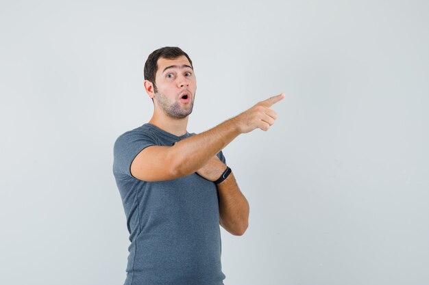 Young male in grey t-shirt pointing away and looking surprised  