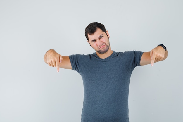 Free photo young male in grey t-shirt pointing down and looking gloomy