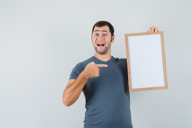 Молодой мужчина в серой футболке указывает на пустую рамку и выглядит веселым