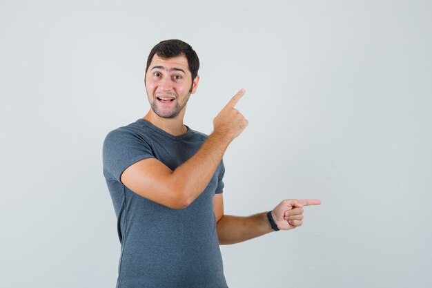 Young male in grey t-shirt pointing up and aside and looking hesitant  