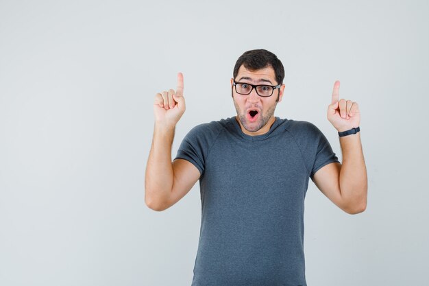 Young male in grey t-shirt pointing up and looking amazed  