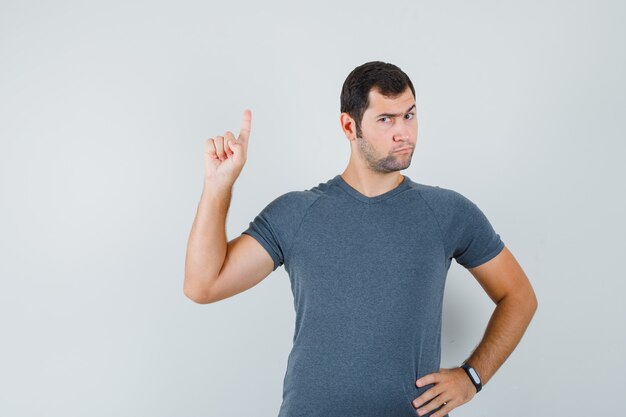 Young male in grey t-shirt pointing up and looking serious  