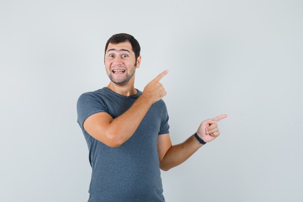 Young male in grey t-shirt pointing at upper right corner and looking merry  