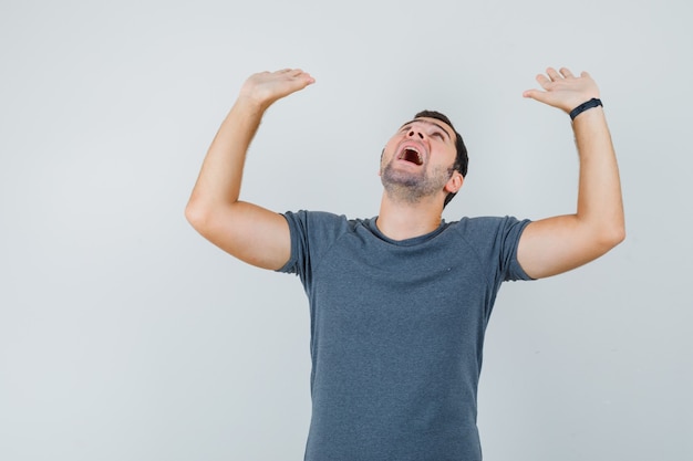 Free photo young male in grey t-shirt raising palms in preventive manner and looking frightened