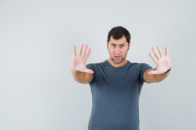 Young male in grey t-shirt showing refusal gesture and looking resolute  