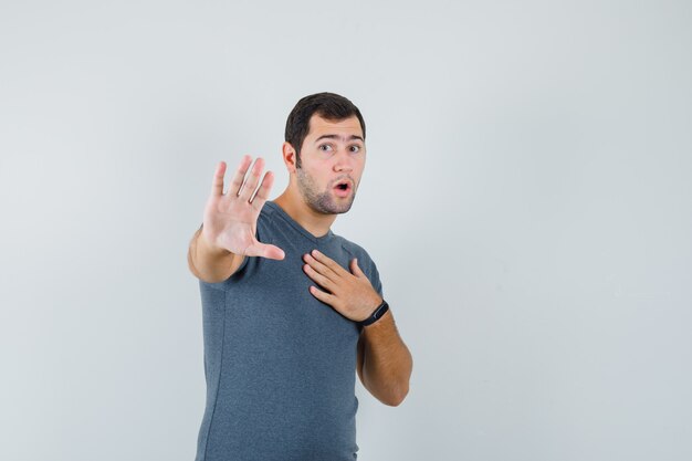 Young male in grey t-shirt showing stop gesture and looking scared  