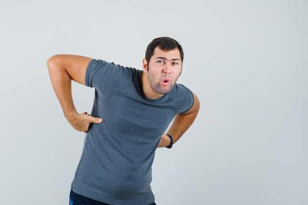 背中の痛みに苦しんでいる灰色のTシャツを着た若い男性