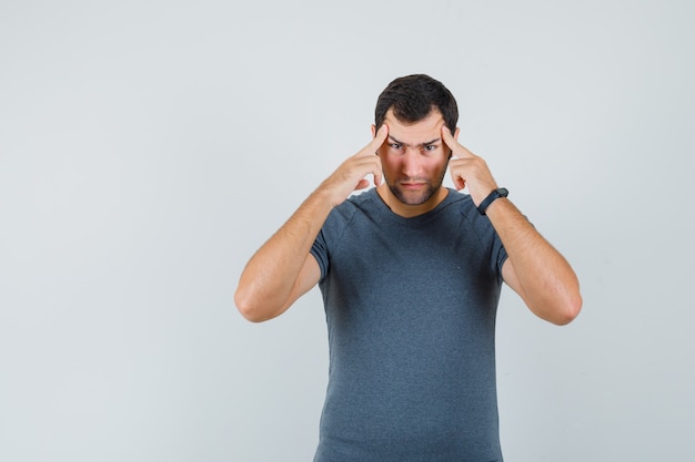 Young male in grey t-shirt suffering from strong headache and looking exhausted  