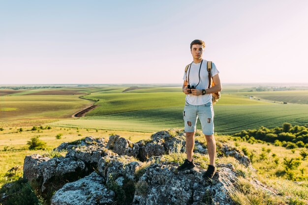 バックパックと双眼で緑の景色を探索する若い男性の登山人