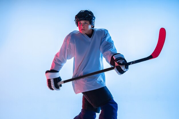 Young male hockey player with the stick on blue wall in neon light