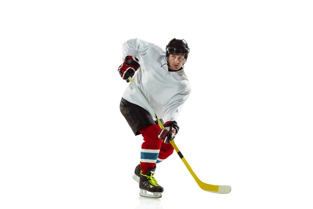 Молодой хоккеист мужского пола с клюшкой на ледовой площадке и белой предпосылке.